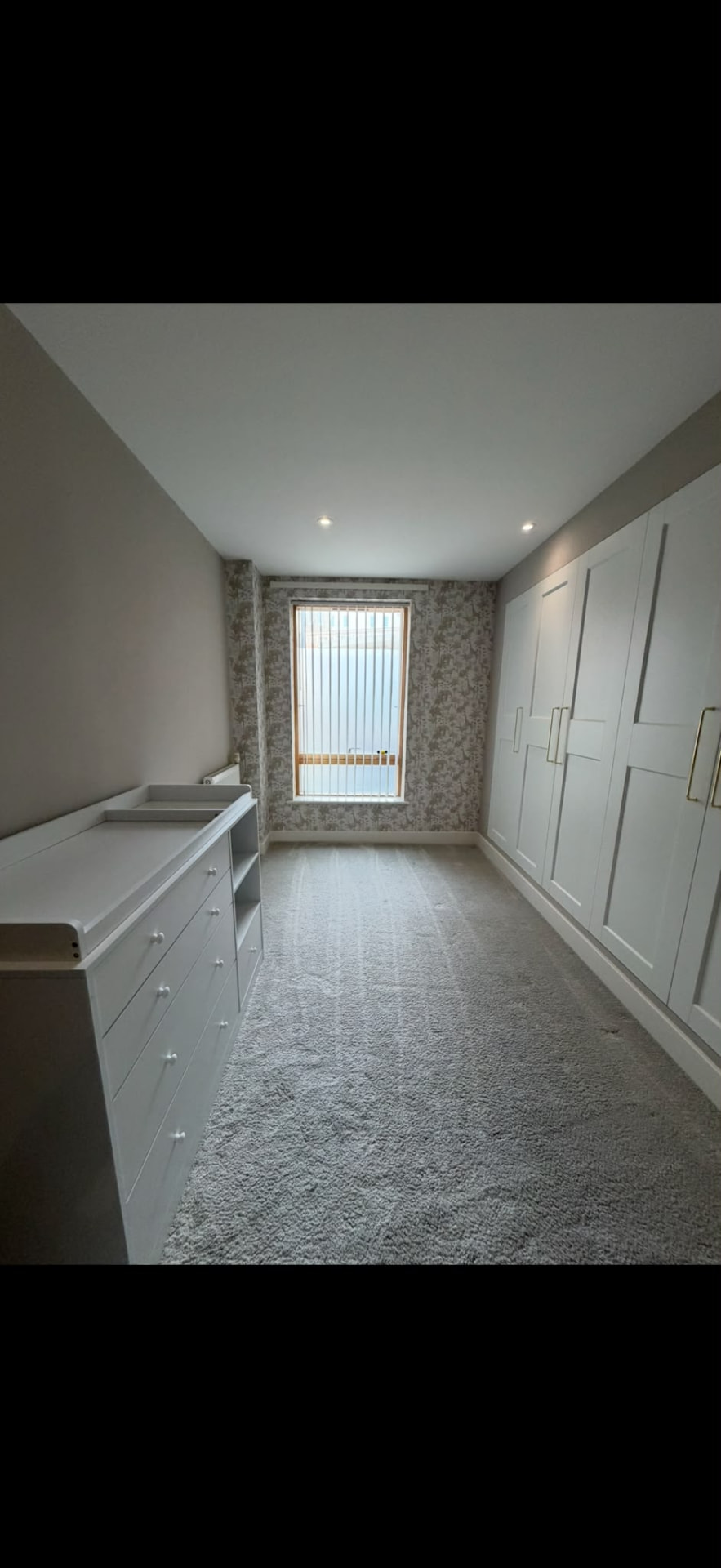 Nursery painted in soft greige with a patterned feature wall and fitted white wardrobes, Hove